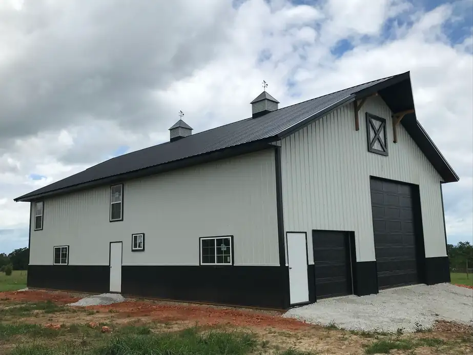 A grey and black pole barn with two black overhead doors, installed by Integrity Overhead Door
