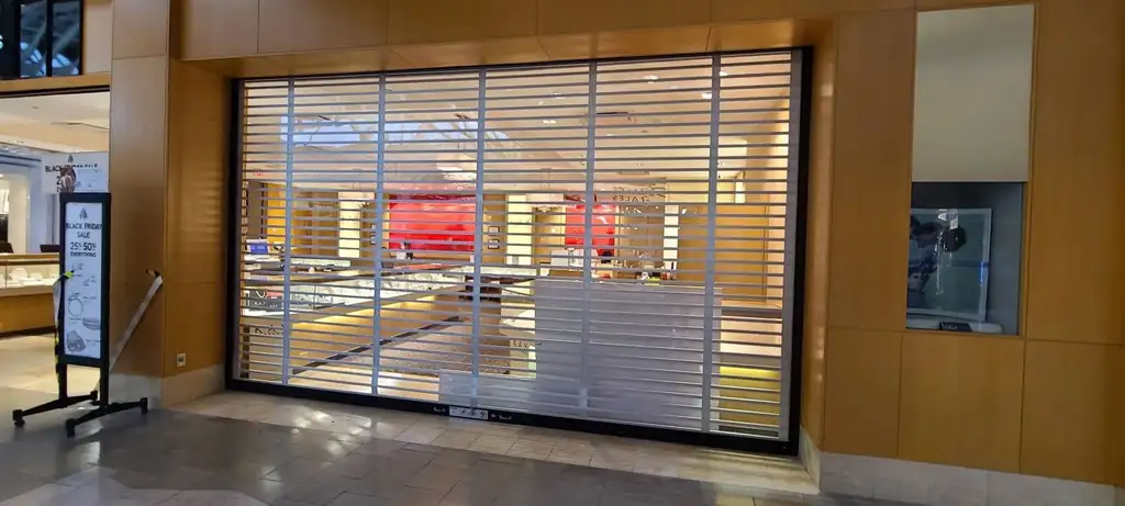 Clear-view security grille closed over a retail storefront, installed by Integrity Overhead Door