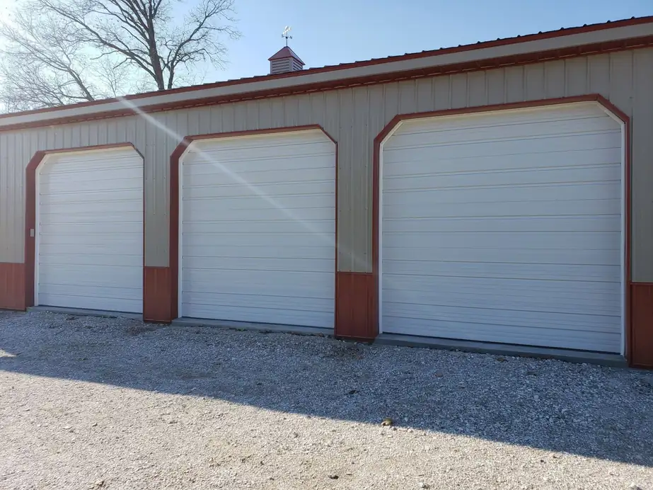 Three white doors with red-brown trim on a tan pole building, installed by Integrity Overhead Door