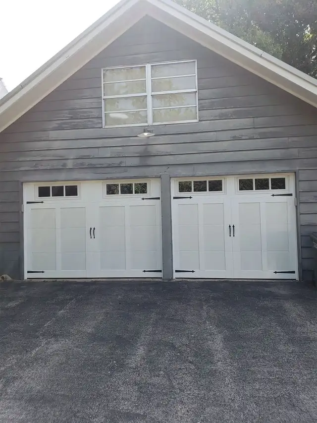 Two white carriage doors with black strap hinges on a grey-sided garage, installed by Integrity Overhead Door