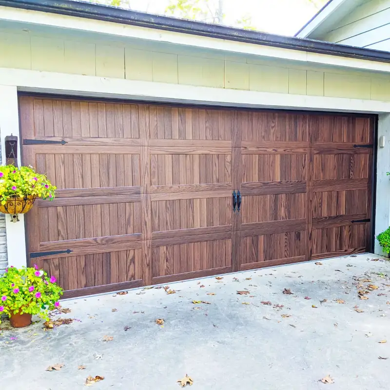Woodgrain carriage double door with black hardware under a hanging flower basket, installed by Integrity Overhead Door