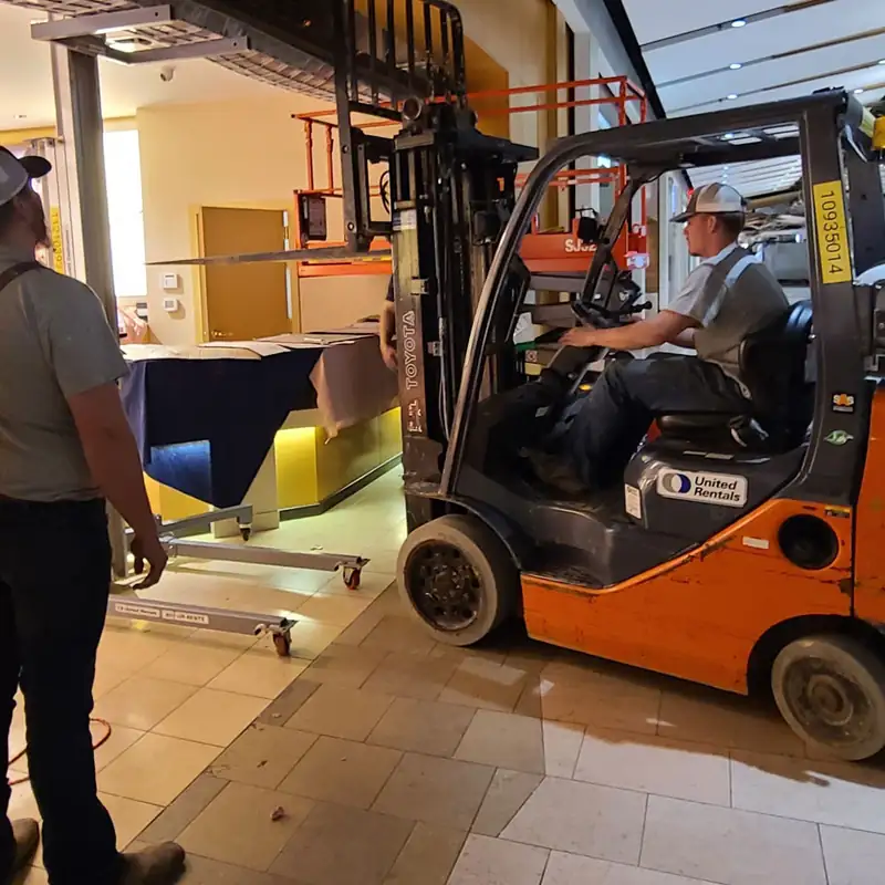 Two crew members moving door material on a forklift at a commercial storefront grille install, installed by Integrity Overhead Door
